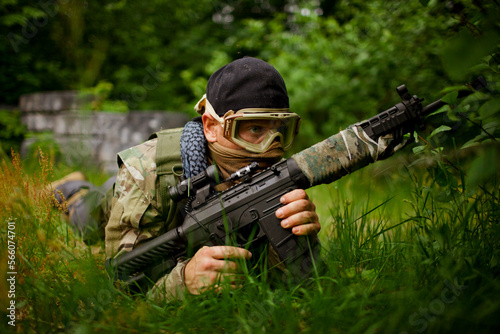 A soldier holds a gun while hiding in thick grass.