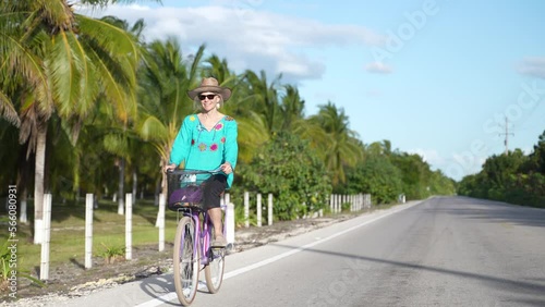Wallpaper Mural Camera comes around to the the front of a pretty mature senior woman riding a bike in a tropical setting with palm trees wearing ethnic clothing and hat. Torontodigital.ca