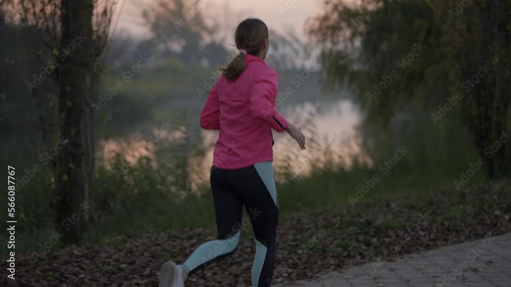 Slow-motion shot of a beautiful woman jogging in the forest near a river Slow-motion shot of a beautiful woman jogging in the forest near a river