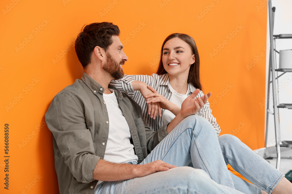 Happy designers sitting on floor near freshly painted orange wall Happy designers sitting on floor near freshly painted orange wall