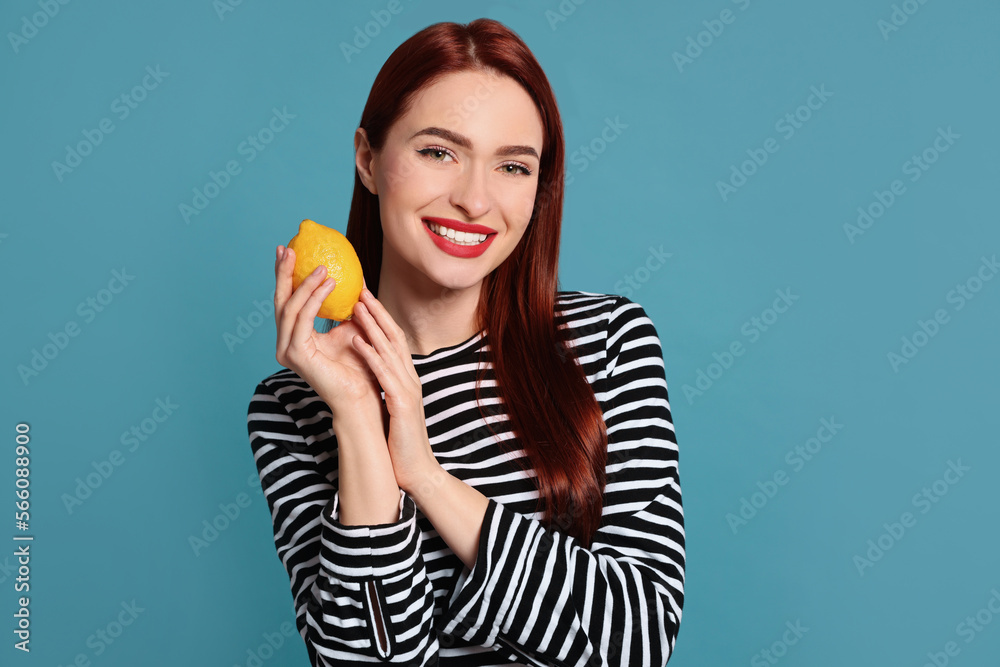 Happy woman with red dyed hair holding whole lemon on light blue background Happy woman with red dyed hair holding whole lemon on light blue background