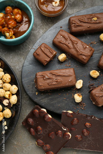 Delicious chocolate candy bars with caramel and nuts on grey table, flat lay