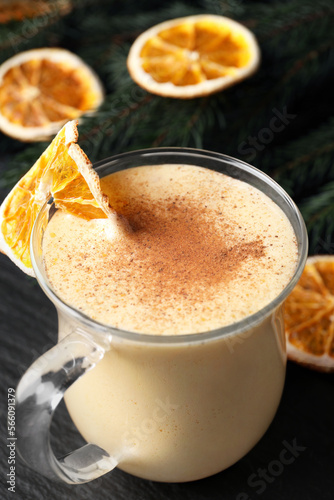 Glass cup of delicious eggnog with dried orange slice and cinnamon on gray table, closeup