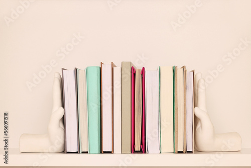 Beautiful hand shaped bookends with books on shelf near beige wall photo