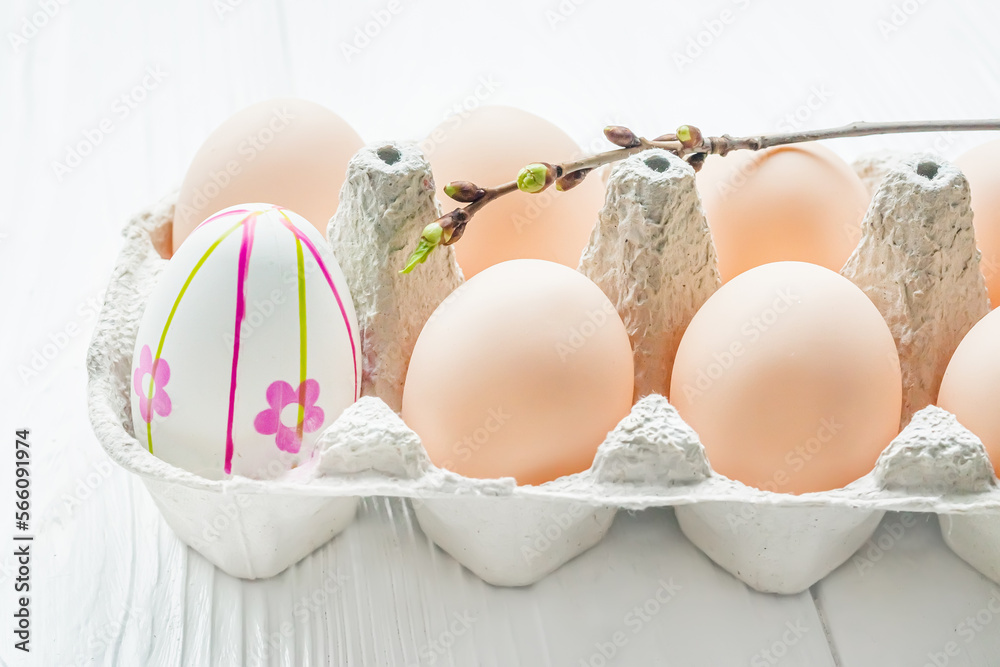 Easter eggs in egg carton. One egg painted by hand and cherry branch with buds that blossom Easter eggs in egg carton. One egg painted by hand and cherry branch with buds that blossom