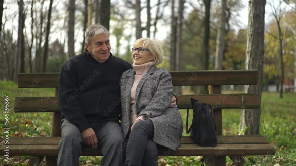 Wide shot of happy loving mature couple resting outdoor on a bench and talking in the forest park Wide shot of happy loving mature couple resting outdoor on a bench and talking in the forest park