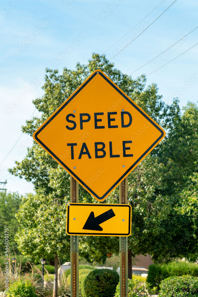 Road sign that says speed table with black and yellow paint on exterior in late afternoon shade in summer sunlight