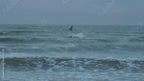 Man engaged in kitesurfing, overcast winter day, high waves, Baltic Sea Karosta beach (Liepaja), slow motion jump, wide distant shot