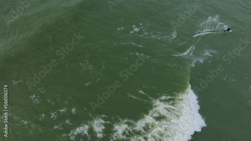 Establishing aerial birdseye view of a man engaged in kitesurfing, overcast winter day, high waves, extreme sport, Baltic Sea Karosta beach (Liepaja), drone dolly shot moving right