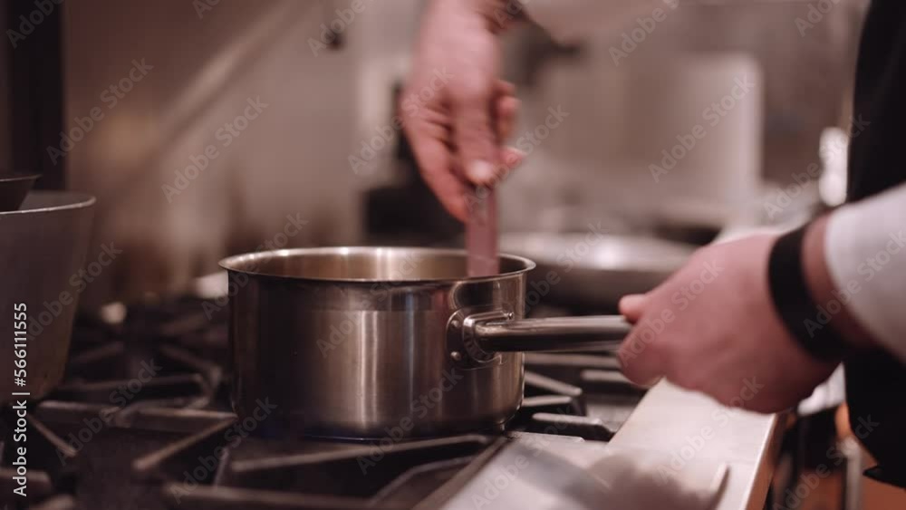 Cook scoops through a saucepan with a spatula while steam comes from a frying pan in the background. Close up shot Cook scoops through a saucepan with a spatula while steam comes from a frying pan in the background. Close up shot