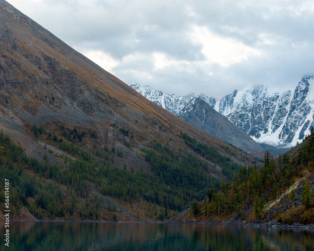 Turquoise lake Shavlinskoe between rocks with trees with snowy peaks and glaciers in the reflection of water in Altai in autumn. Peaks Dream, Fairy Tale, Beauty.