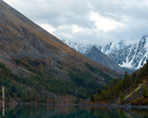 Turquoise lake Shavlinskoe between rocks with trees with snowy peaks and glaciers in the reflection of water in Altai in autumn. Peaks Dream, Fairy Tale, Beauty.