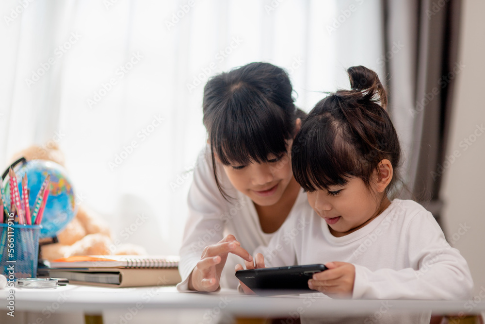 Concept kids and gadgets. Two little girls siblings sisters look at the phone and smile. They hold a smartphone watch videos, learn, play games, speak online. Internet for children. Parental control Concept kids and gadgets. Two little girls siblings sisters look at the phone and smile. They hold a smartphone watch videos, learn, play games, speak online. Internet for children. Parental control