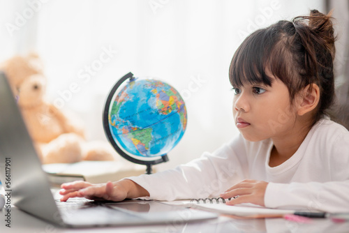Asian schoolgirl doing her homework with laptop at home. Children use gadgets to study. Education and distance learning for kids. Homeschooling during quarantine. Stay at home