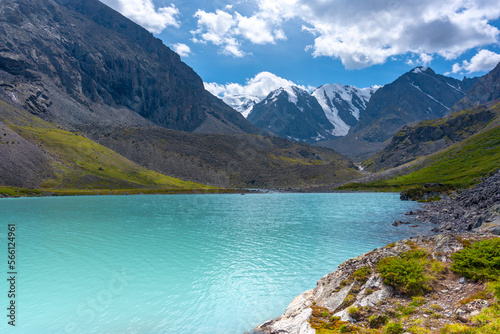 Fototapeta Naklejka Na Ścianę i Meble -  Mountain lake with turquoise water Karakabak in the Altai mountains with snowy peaks and glaciers with under the clouds and green grass with a hanging stone.