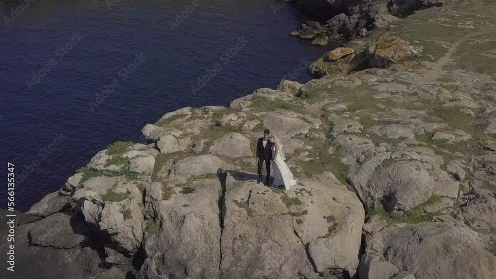 The bride and groom in wedding clothes are walking along the seashore, hugging, kissing, running, enjoying themselves. Husband and wife are filming a clip in a hotel on vacation. Lovely couple look at The bride and groom in wedding clothes are walking along the seashore, hugging, kissing, running, enjoying themselves. Husband and wife are filming a clip in a hotel on vacation. Lovely couple look at