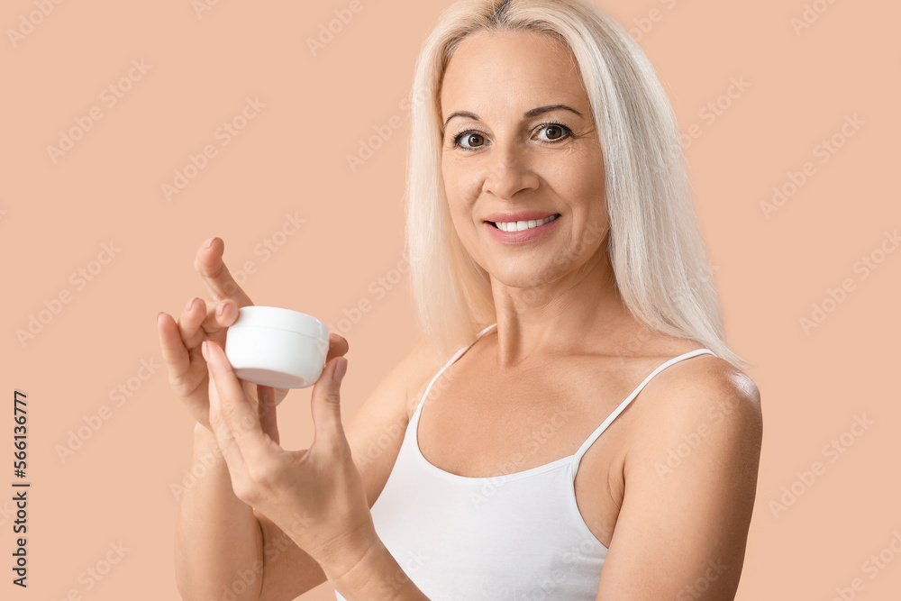 Mature blonde woman with jar of cream smiling on beige background Mature blonde woman with jar of cream smiling on beige background
