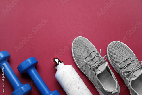 Sports water bottle with dumbbells and sneakers on red background