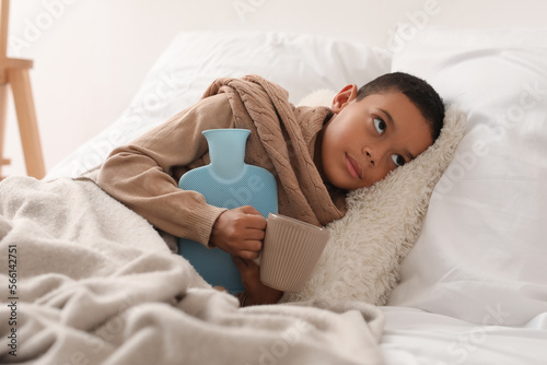 Fotografie, Tablou Ill African-American boy with hot water bottle in bedroom