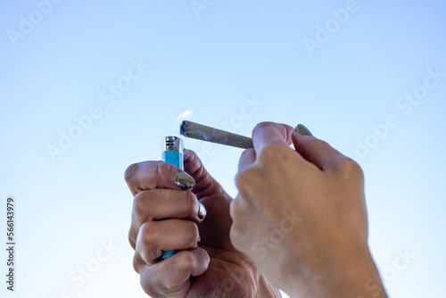 Female model lighting a cannabis joint with the sky in the background