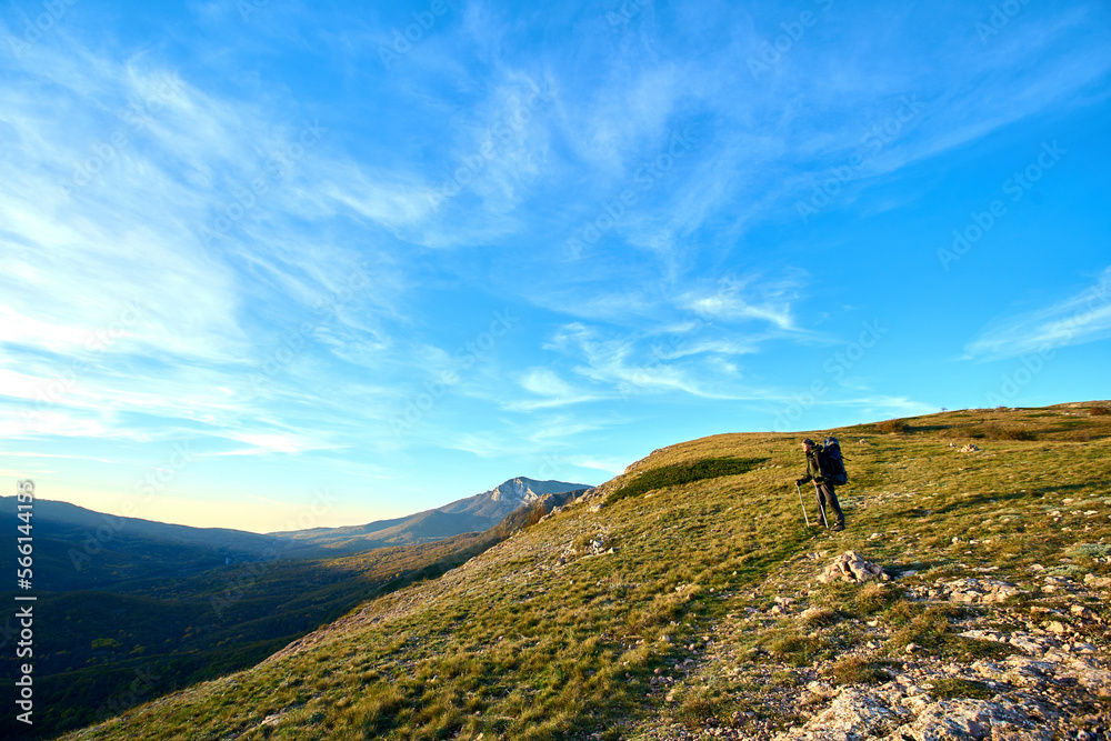 Silhouette of a man in the mountains. Successfully achieving goals. Male hiker on mountain peak with green grass looking at beautiful mountain valley at sunset against clear blue sky.. Silhouette of a man in the mountains. Successfully achieving goals. Male hiker on mountain peak with green grass looking at beautiful mountain valley at sunset against clear blue sky..