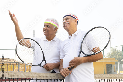 Active senior tennis players meeting at the net after a match and talking. © G-images
