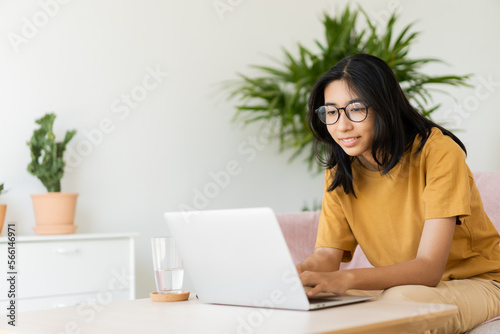 Asian woman wear glasses typing work on laptop computer happy at home