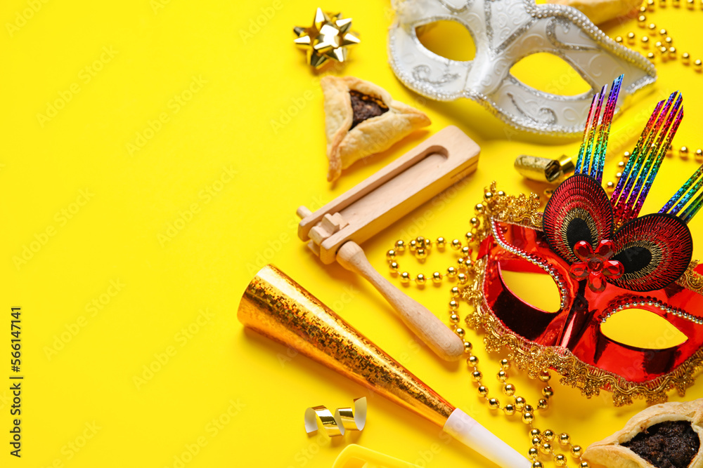 Hamantaschen cookies, carnival masks and noisemakers for Purim holiday on yellow background