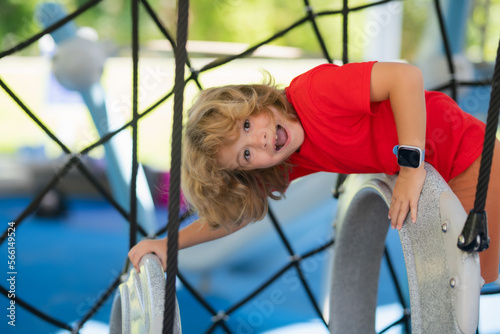 Child climbs up in a park on a playground on a summer day. Childrens playground in a public park. Recreation for children. Kid hanging at outdoor playground.