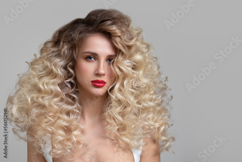 Beautiful curly blonde woman with long hair and bright makeup. Grey background