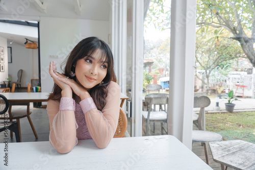 Free Download Thoughtful Asian woman keeps hand on chin looks pensively above dressed in pink dress poses thinks about future - GFXLoad