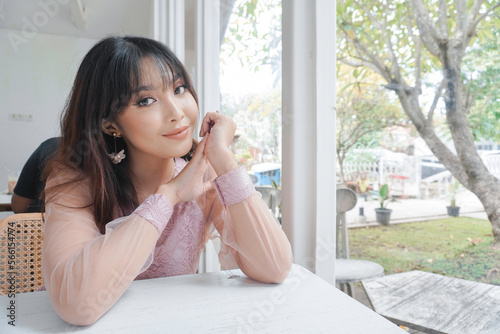 A smiling Asian woman wearing pink dress while sitting near window Free Download A smiling Asian woman wearing pink dress while sitting near window - GFXLoad