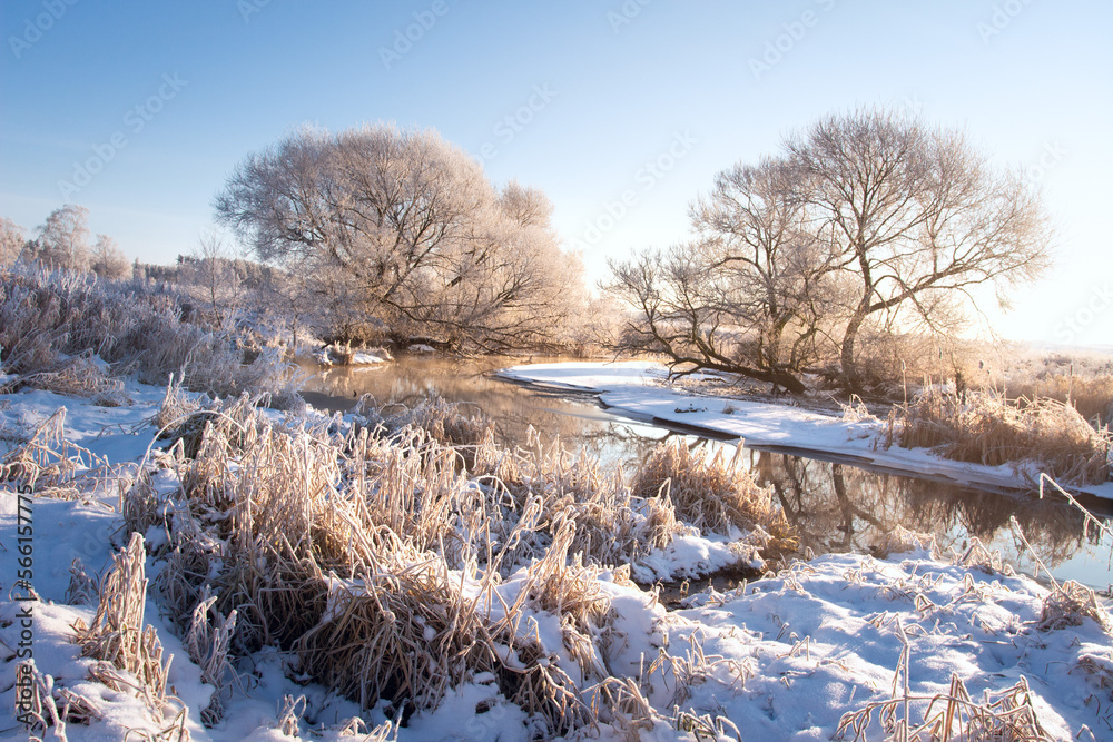 Amazing landscape of the river bank and meadow near. Dry grass covered with snow on the beach river. All nature in hoarfrost. Over river are light mist.