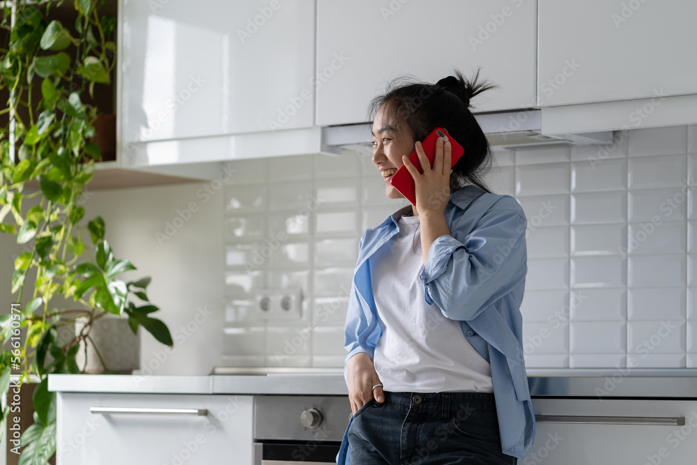 Cheerful carefree Asian girl talking on phone with college friends standing in kitchen at home. Optimistic joyful Korean woman making call via smartphone and laughing discussing plans for Sunday walk Cheerful carefree Asian girl talking on phone with college friends standing in kitchen at home. Optimistic joyful Korean woman making call via smartphone and laughing discussing plans for Sunday walk