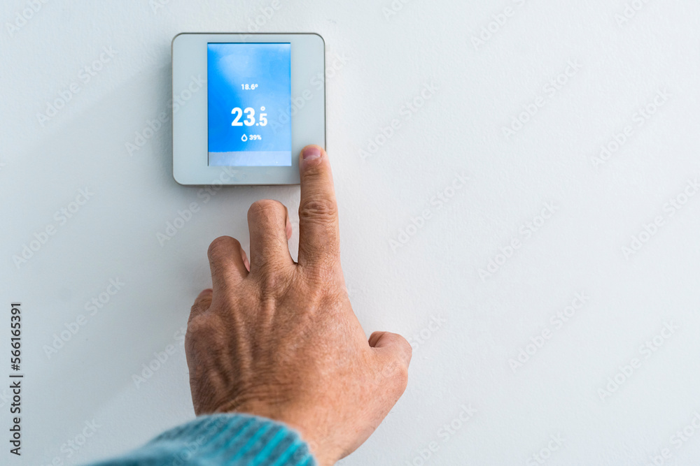 Hand of man adjusting thermostat on wall Hand of man adjusting thermostat on wall