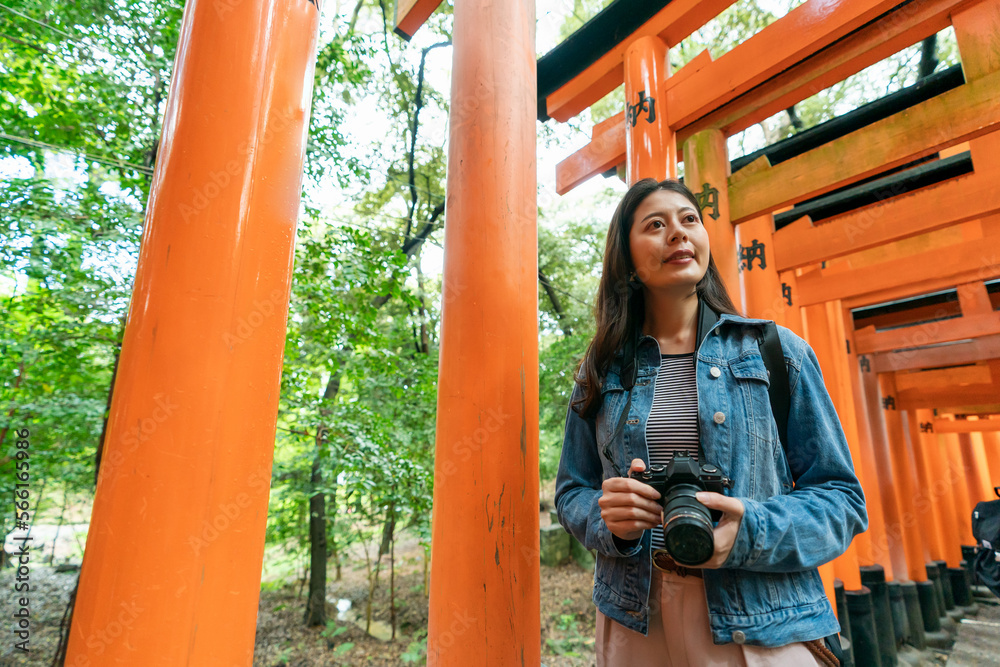 cheerful asian Japanese female traveler enjoying scenic view and historic site while taking senbon torii hike to fushimi inari Taisha shrine in Kyoto japan. translation: âofferingâ