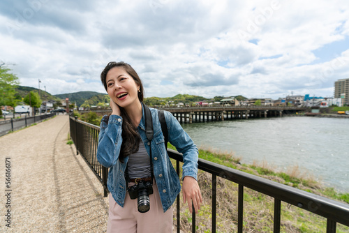 cheerful asian Japanese girl visitor resting arm on metal railing and holding her blowing hair on a windy day while relaxing near uji river in Kyoto japan © PR Image Factory