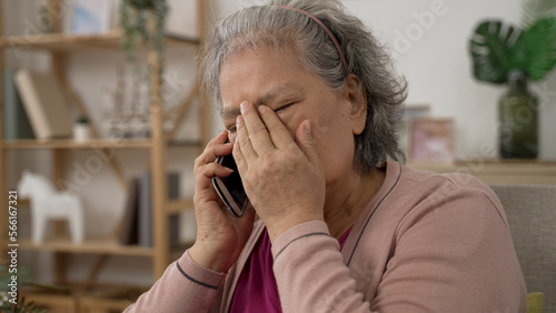 shoulder shot of a sad asian grandma covering her face in agony on receiving a terrible news on the mobile phone in the living room at home.
