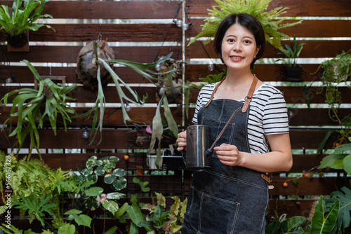 portrait of beautiful asian korean girl flower shop assistant carrying a watering can and looking at camera with smile on fresh house plant background