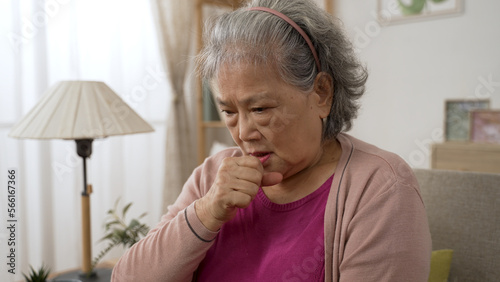 closeup view of an unwell asian grandma getting lung infection is patting on her chest while coughing in the living room at home