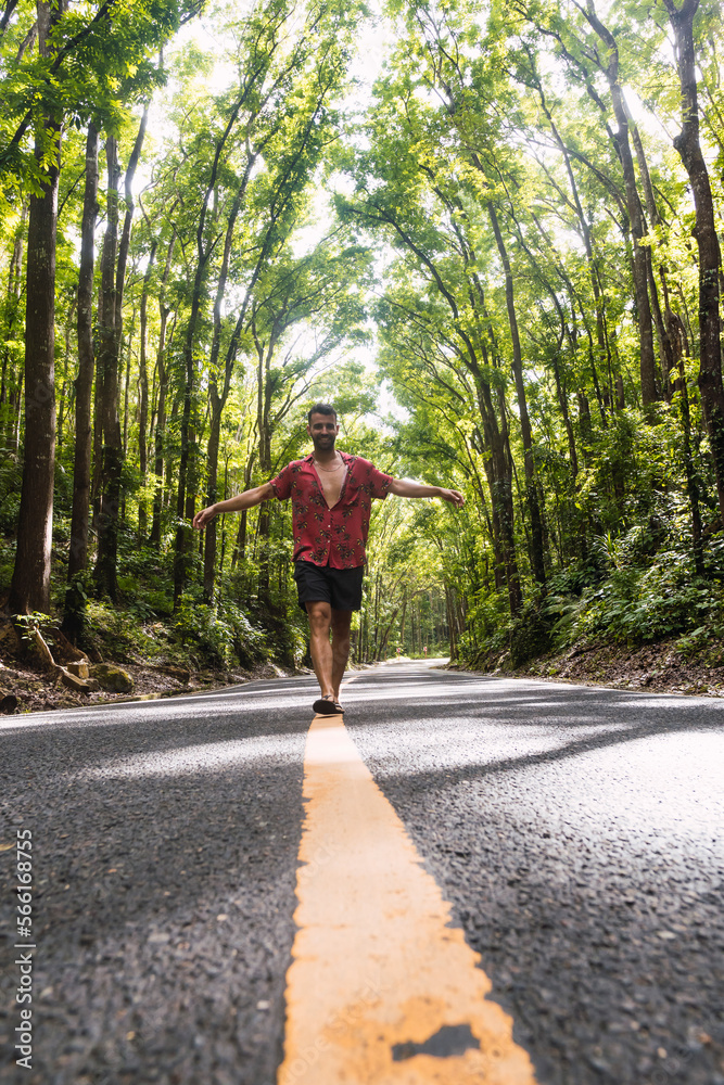 Man walking on road marking in front of trees
