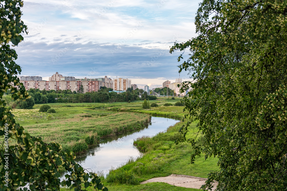 A green field with a small river can be seen the outskirts of the city