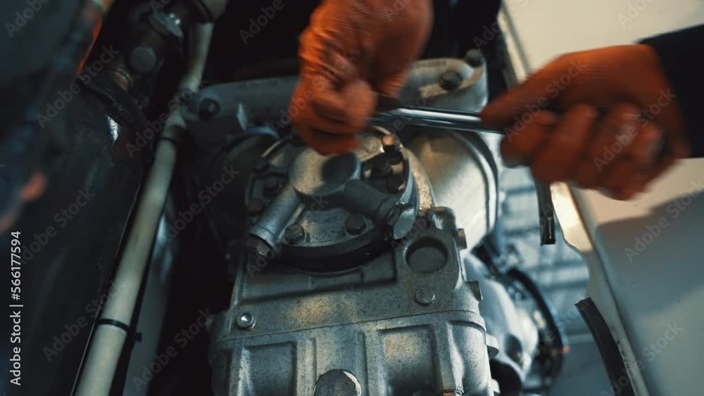 mechanic with orange gloves ties down bolts with a wrench key of a cover from a small engine. Reefer trailer components