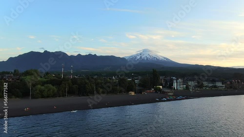 Aerial approach towards shore of Villarrica Lake in Pucon, Chile with towering Villarrica Volcano in background. Beautiful Chilean Andes mountain establishing shot. photo