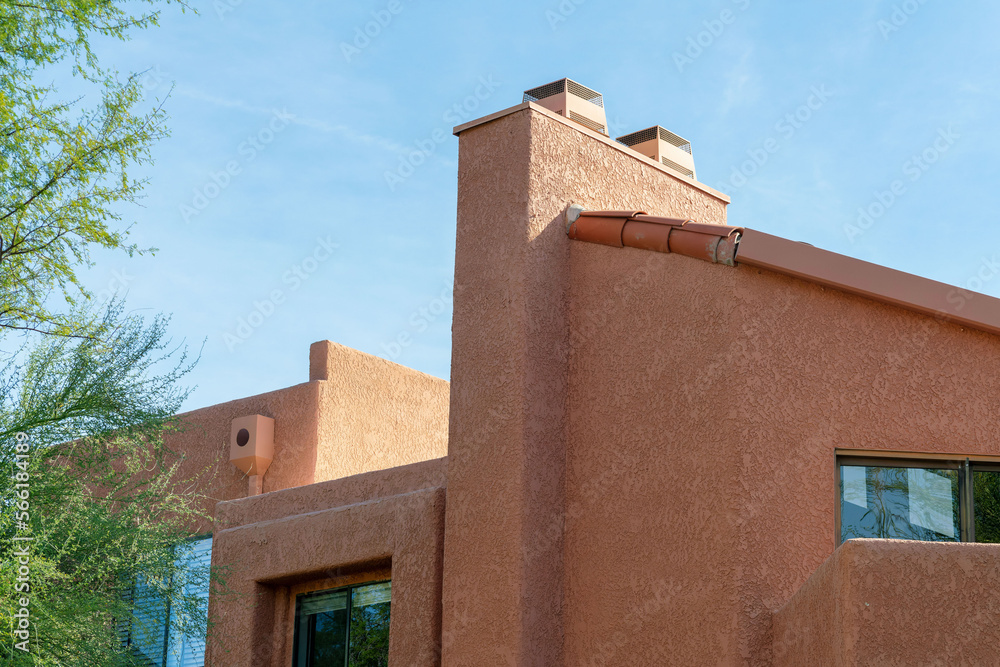 Modern adobe style building with orange exterior cement stucco with windows and front yard trees Modern adobe style building with orange exterior cement stucco with windows and front yard trees