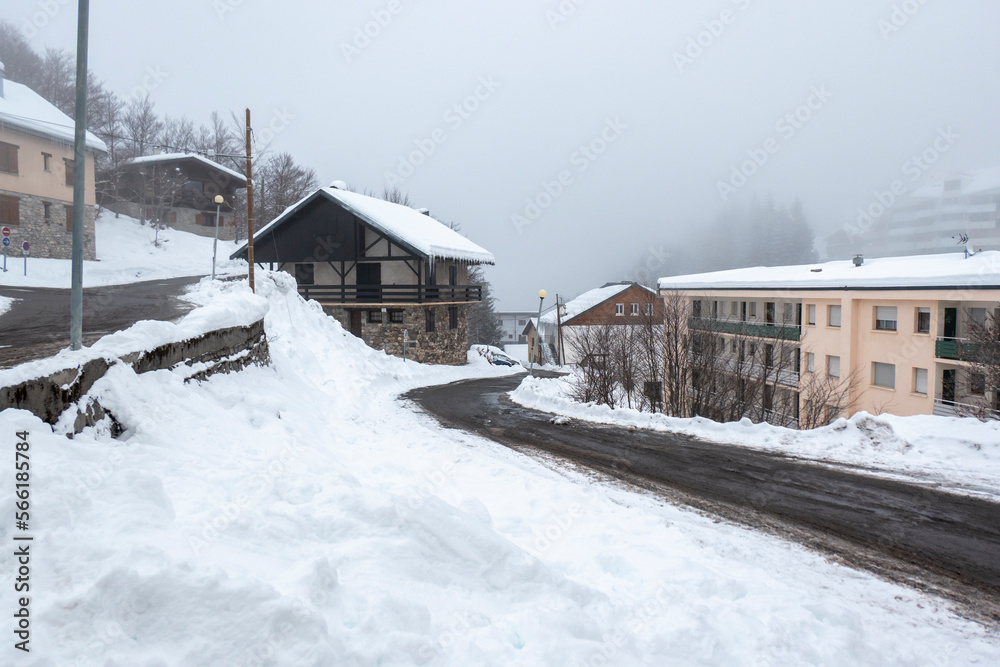 Estrada a meio de uma vila coberta por muita neve e nevoeiro num dia frio de inverno em Gourette, Pirenéus Atlânticos, França
