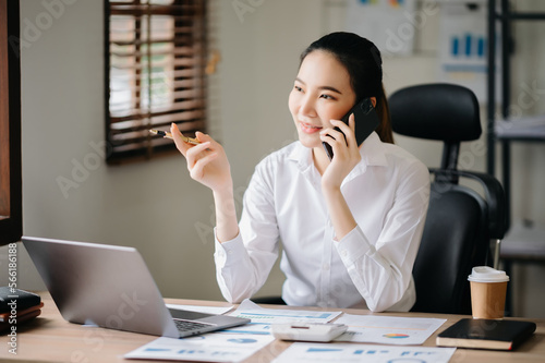 Business asian woman Talking on the phone and using a laptop with a smile while sitting at office..