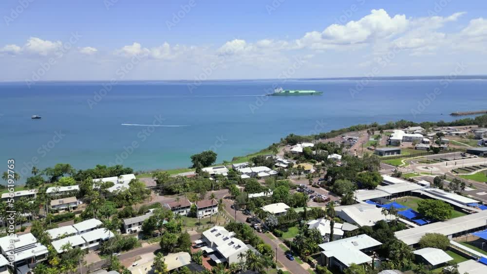 Aerial Drone over properties in residential neighbourhood suburb. Birds eye view of house roofs Tropical greenery palm trees grass. Skyline of ocean and beach ship in harbour Aerial Drone over properties in residential neighbourhood suburb. Birds eye view of house roofs Tropical greenery palm trees grass. Skyline of ocean and beach ship in harbour