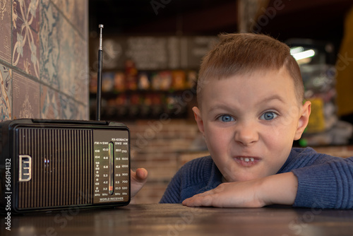 Konstfotografi Charming grimacing boy at a table in a cafe with an old vintage radio