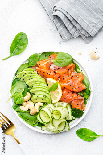 Salmon salad for ketogenic diet with avocado, spinach, cucumber, cashew nuts. Low-carbohydrate lunch rich in healthy fats. White table background, top view